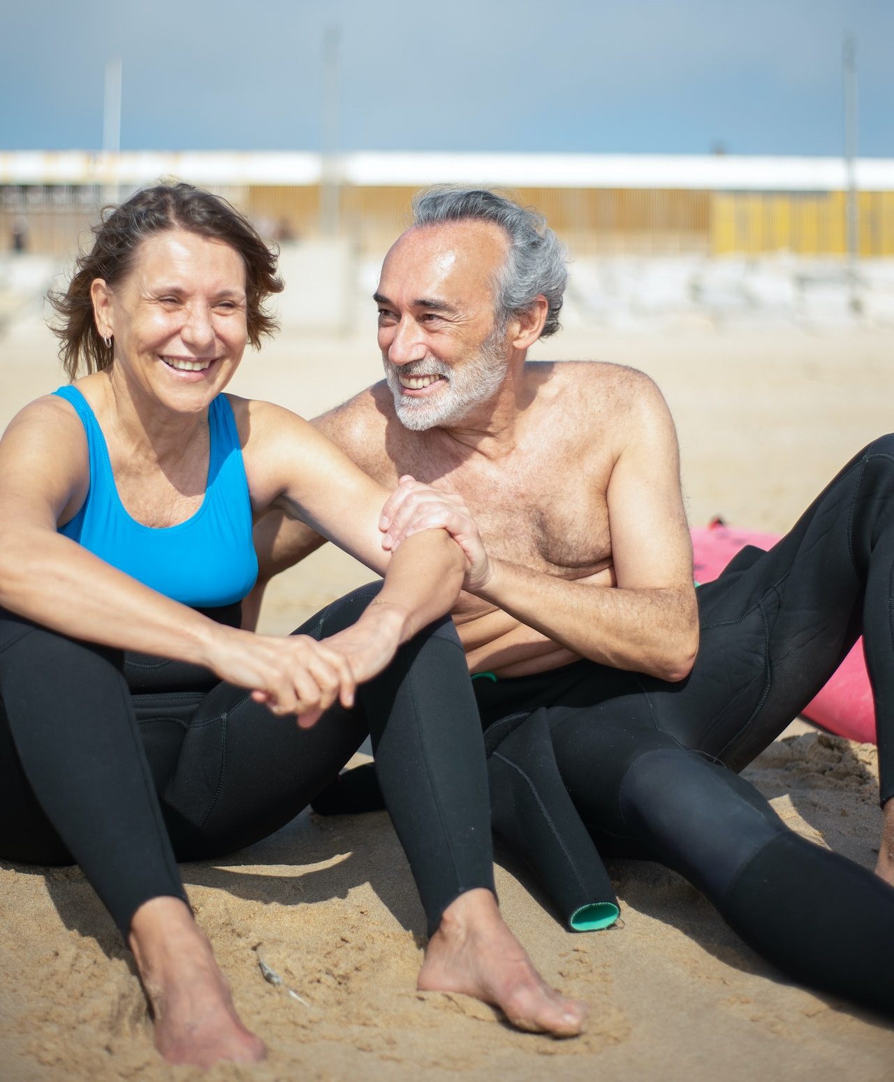 senior man and woman on sunny beach in wetsuits